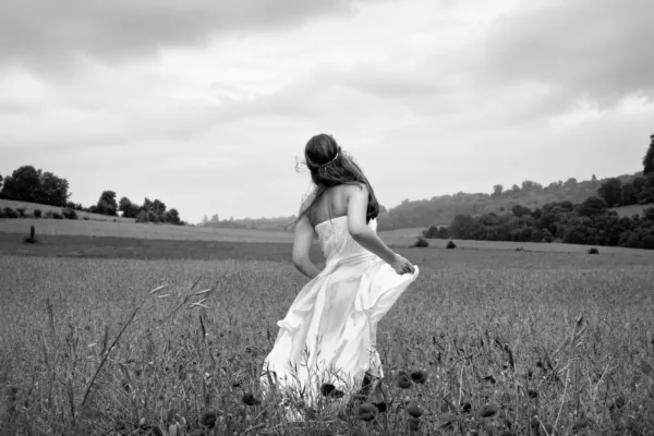Bride walking through a countryside field holding her wedding dress