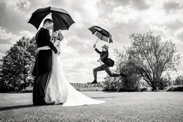 Wedding couple under an umbrella as a guest jumps through the air beside them