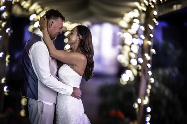 Bride and groom embracing beneath decorative lights during their evening wedding celebrations.