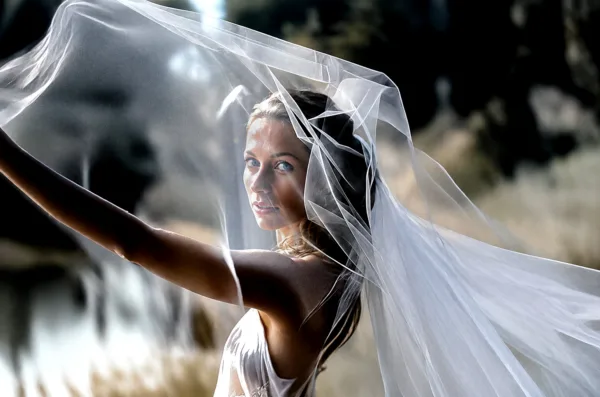 Bride holding her flowing veil above her head in strong natural light