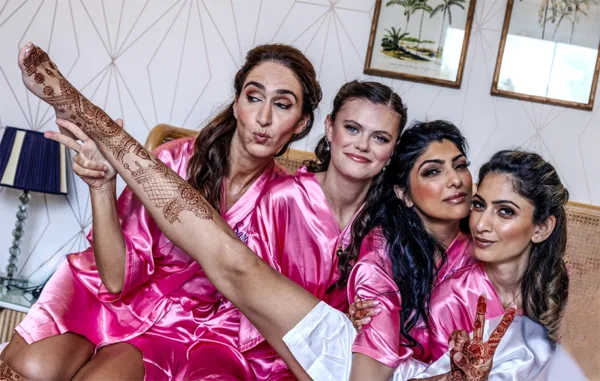 Bridal party in pink robes displaying intricate henna during wedding preparations.