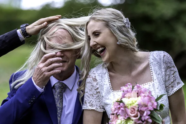 Bride laughing with a wedding guest as her hair blows across his face.