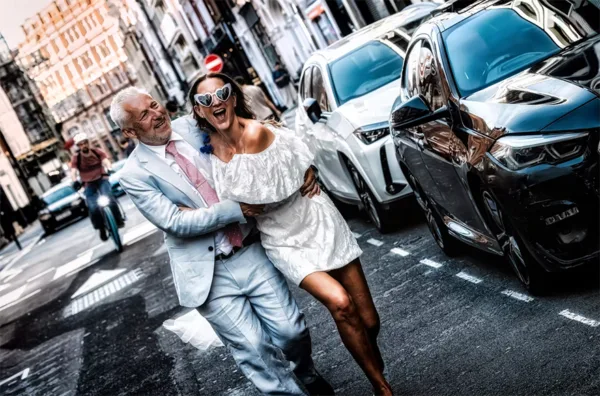 Stylish wedding couple laughing and running together through a city street.