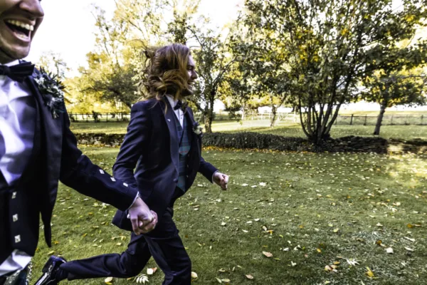 Two grooms running hand in hand outdoors during their wedding celebration.