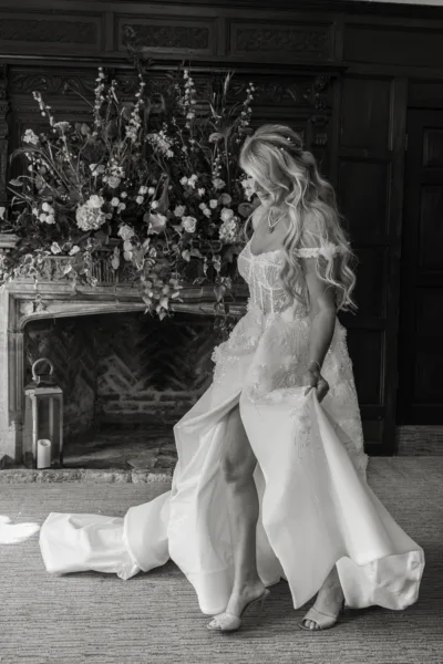 Black-and-white bridal portrait beside a flower-filled ornate fireplace.