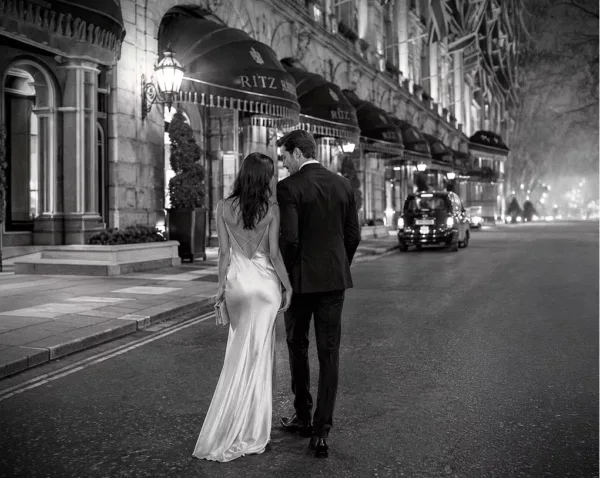 Elegantly dressed wedding couple walking together outside The Ritz London at night.