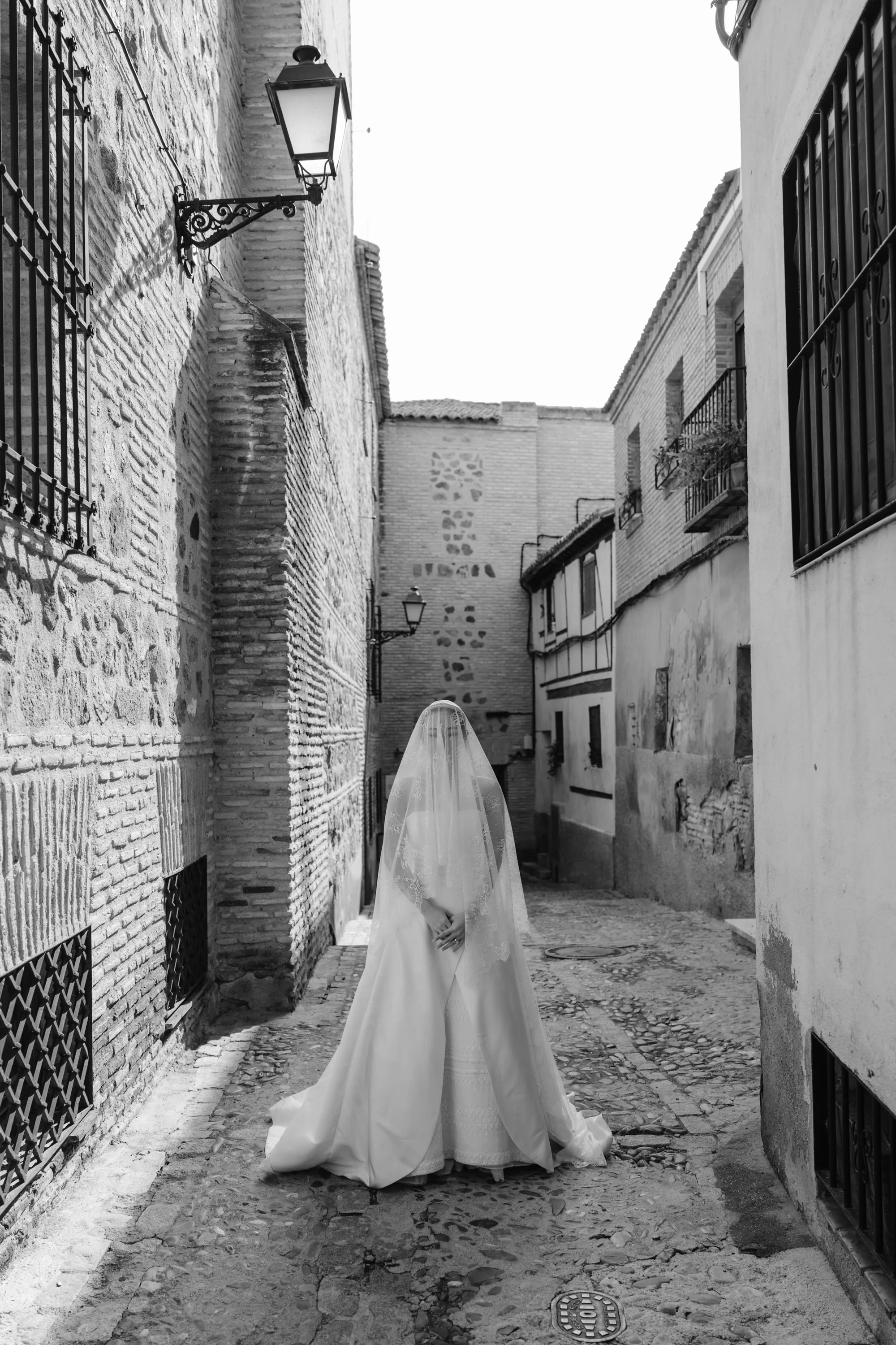 Wedding Toledo Spain Sam Sparks Photography 95 - A Multicultural Wedding in Toledo, Spain, with Korean Heritage and Deep Southern Roots Black and white image of bride wearing a thrifted Maggie Sottero wedding dress and veil over her face. She stands in the streets of Toledo in Spain.