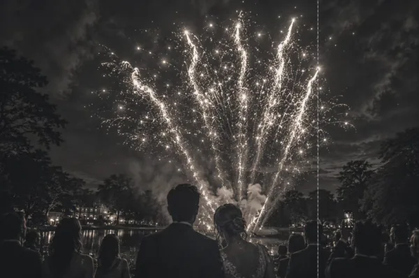 Bride and groom viewed from behind watching a dramatic wedding fireworks display over a lake at night.