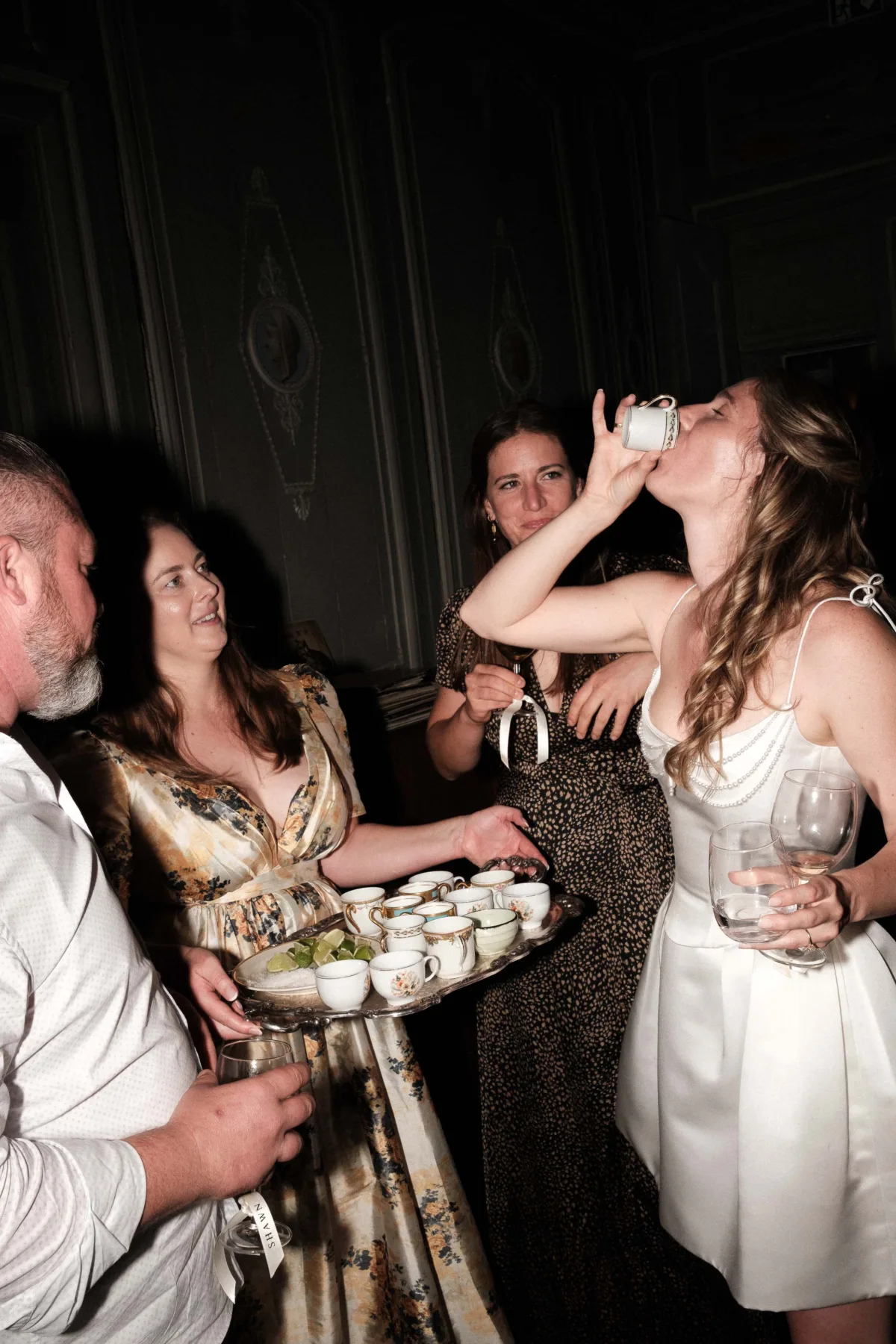 Bride in a short dress drinking shots from a china tea cup on the evening of her wedding.
