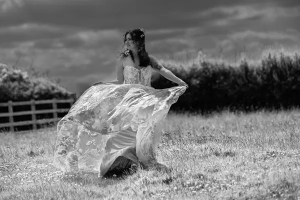 Bride holding her flowing floral wedding dress in a countryside meadow.