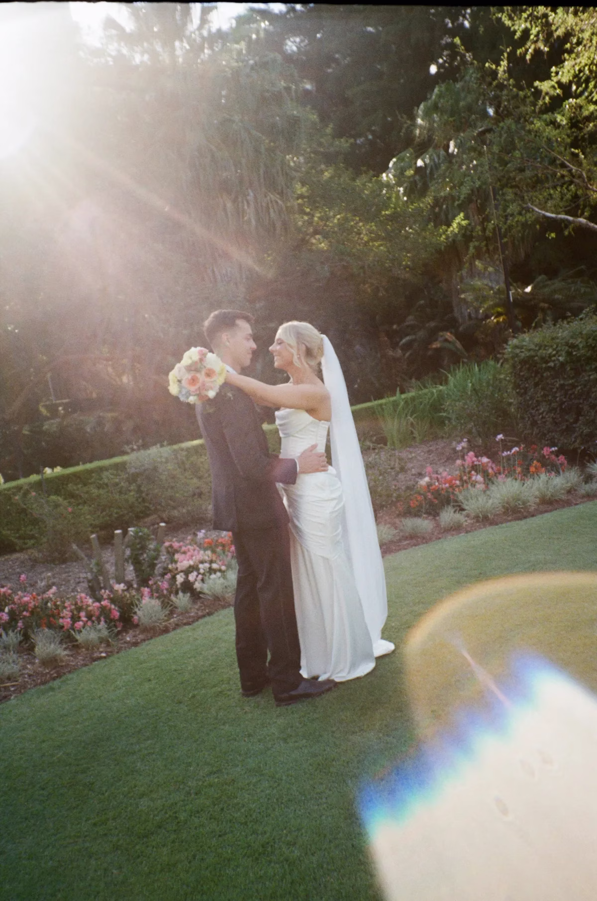 TheLightPhoto Film LoveMyDressParnership 10 1200x1810 1 - The Light Photo & Film: 35mm Wedding Photography and Super 8 for Creative Couples Bride and groom standing together in a garden with sunlight streaming through the trees.