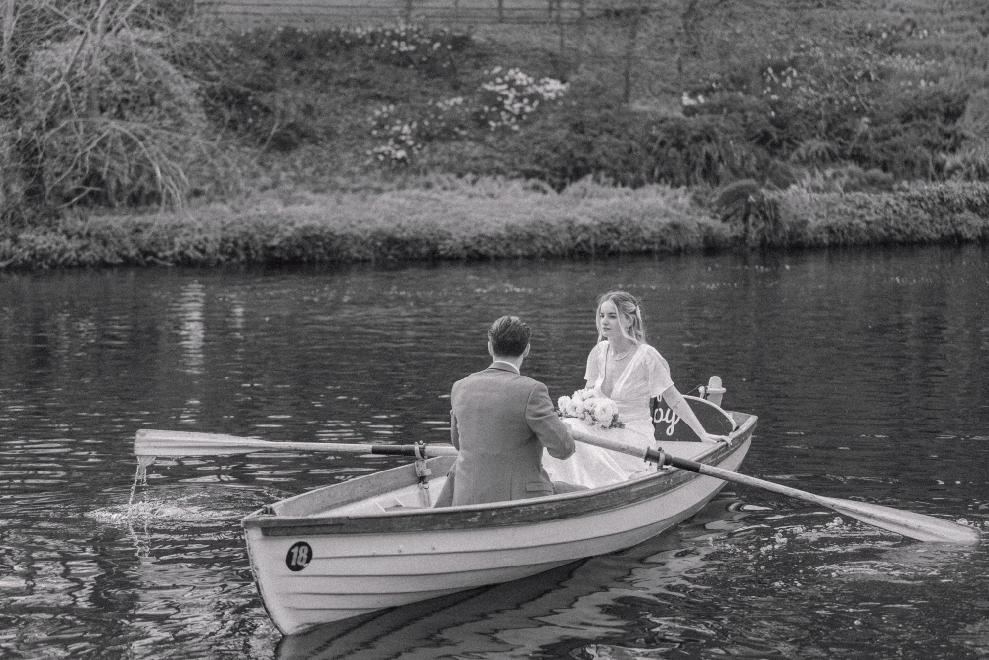 Black and white photograph of a groom rowing a boat with his bride inside.