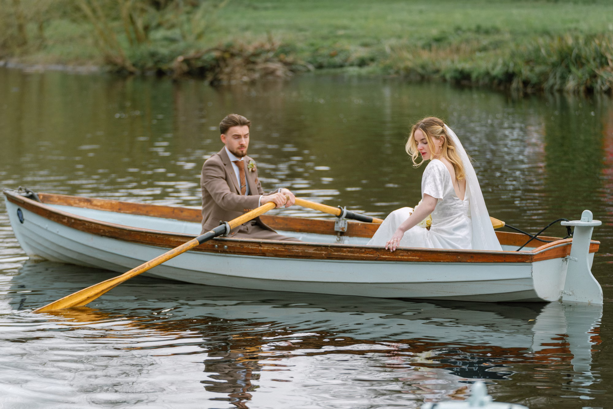 Groom rowing a pale blue boat along the river in Knaresborough, with the bride seated opposite in her gown and veil