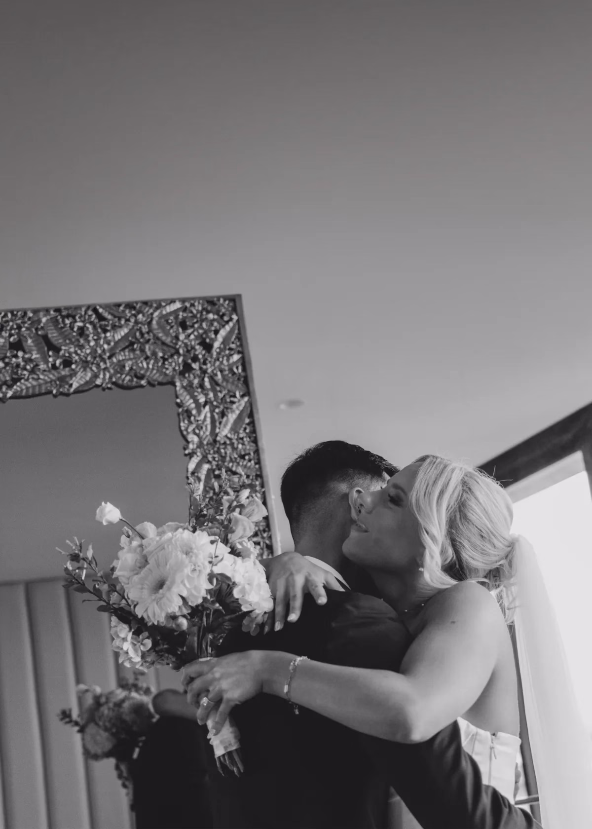 bride groom kissing beside mirror the light photo and film - The Light Photo & Film: 35mm Wedding Photography and Super 8 for Creative Couples Black and white photograph of a bride and groom kissing beside an ornate mirror, with a bouquet held out to one side.