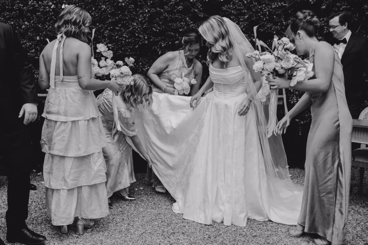 bridesmaids helping bride dress train the light photo and film - The Light Photo & Film: 35mm Wedding Photography and Super 8 for Creative Couples Black and white photograph of bridesmaids helping to arrange the train of a wedding dress outdoors.