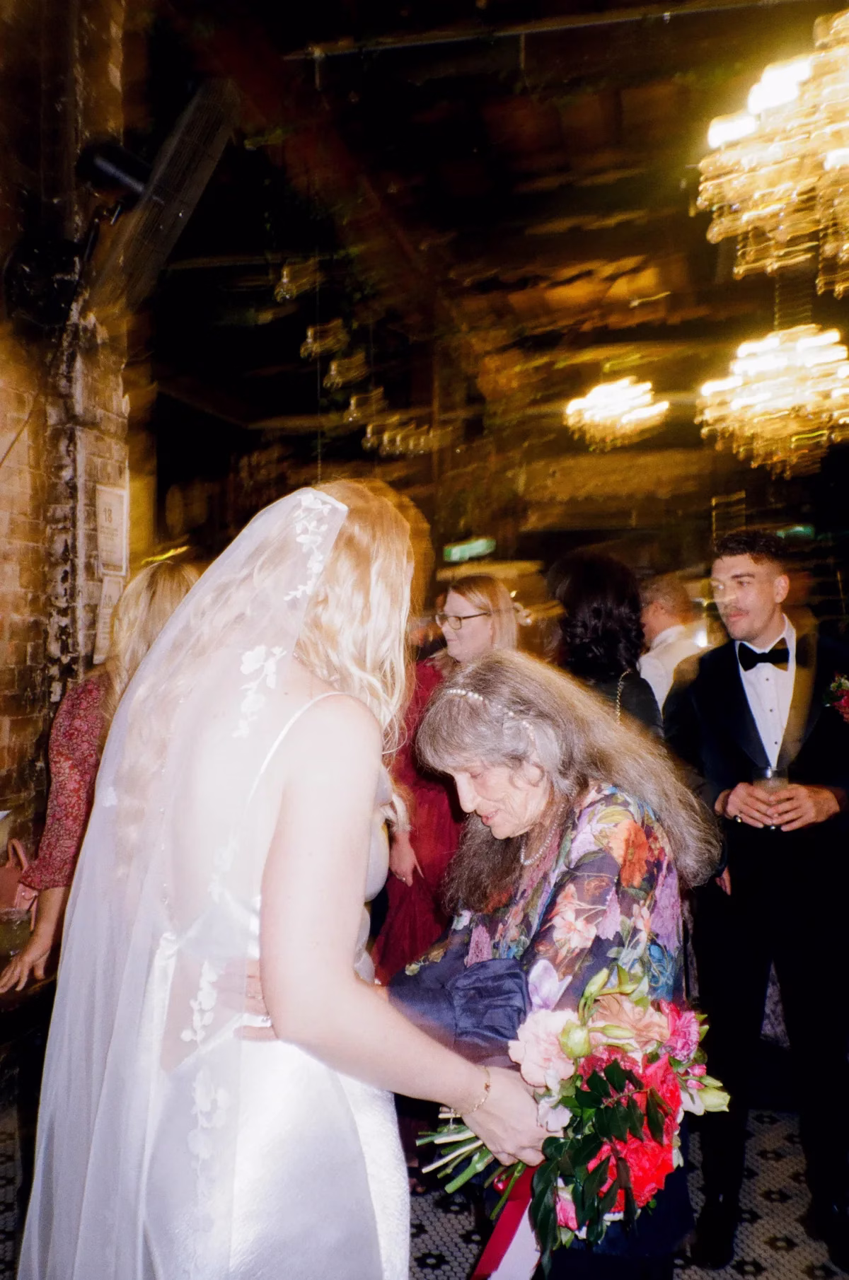 the light photo and film the bride and grandma - The Light Photo & Film: 35mm Wedding Photography and Super 8 for Creative Couples Bride leaning towards an older wedding guest in a floral outfit during the reception.