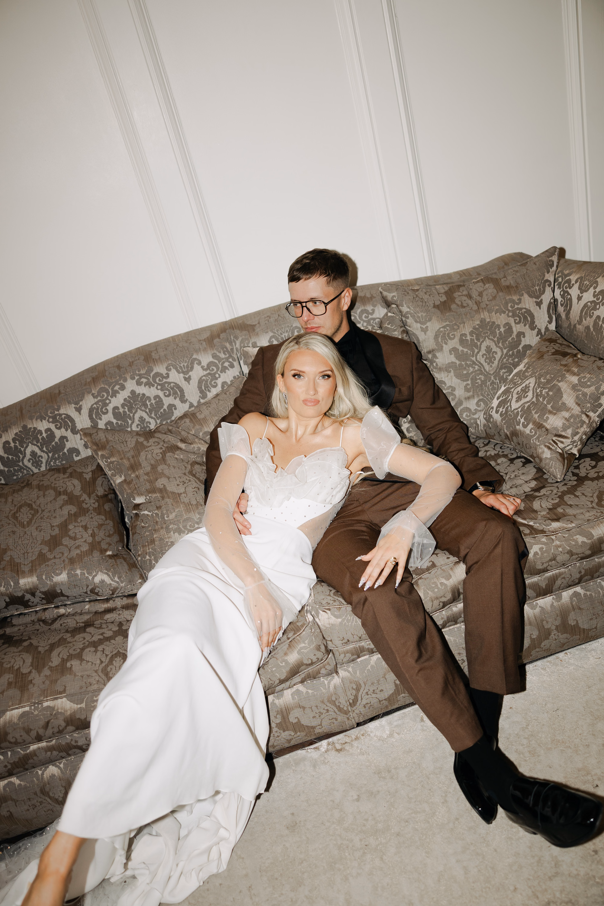 Dalton Old Pump House Wedding Seaham Durham 145 1 - Kate & Jonny's Dalton Old Pump House Wedding With 80 Chandeliers & 3 Dresses Bride wearing Rime Aradaky via the Mews, reclining on a sofa with her groom that wears a brown suit.