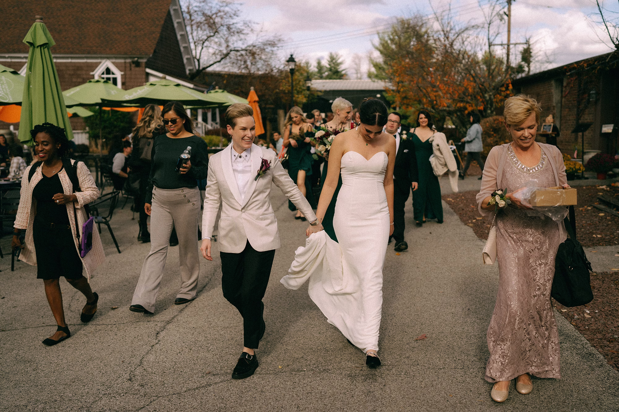 Female LGBTQ newlyweds holding hands as they walk through Brotherhood Winery’s grounds with their wedding guests
