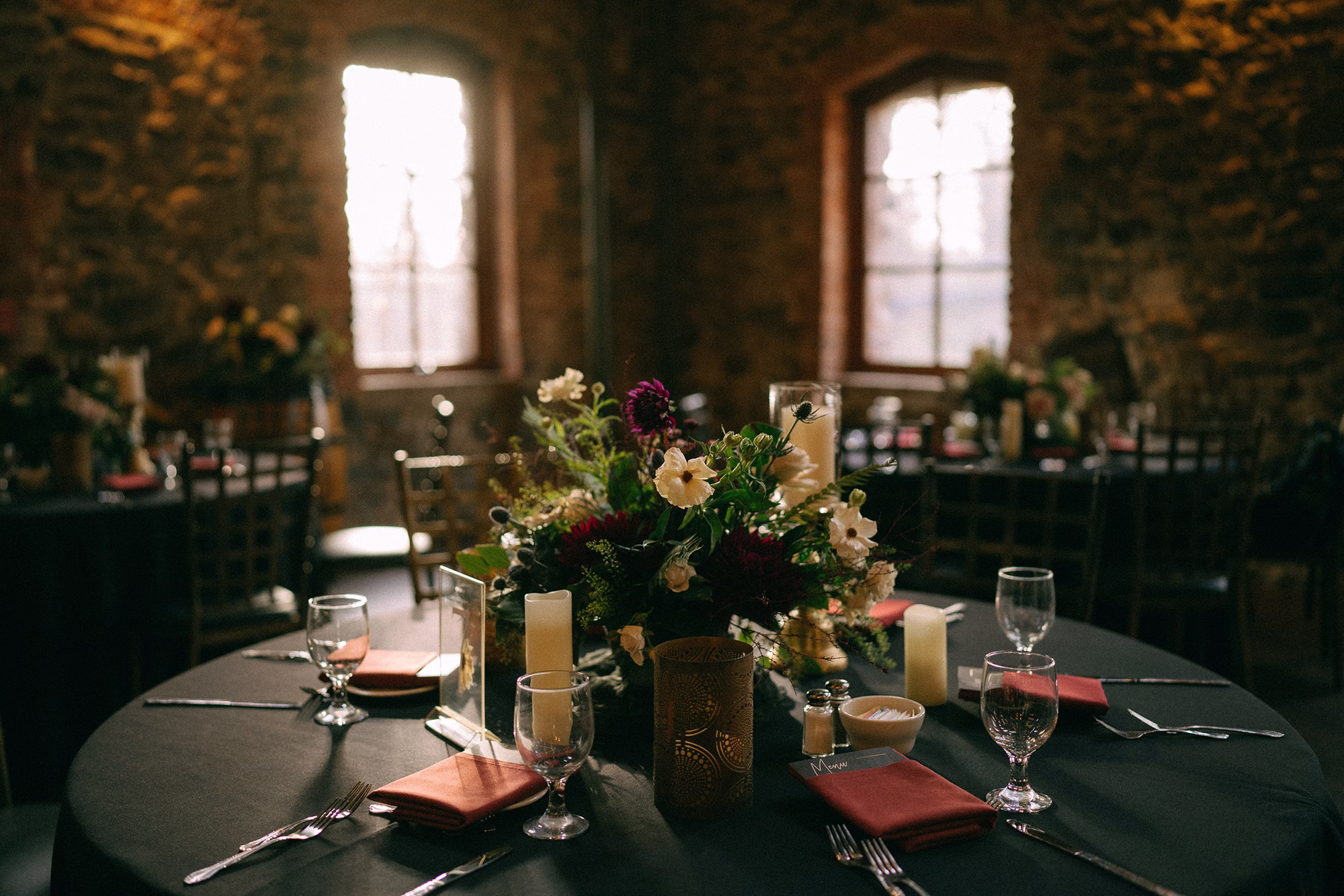 Round reception table with dark green linen, rust-coloured napkins, pillar candles and cream and burgundy flowers