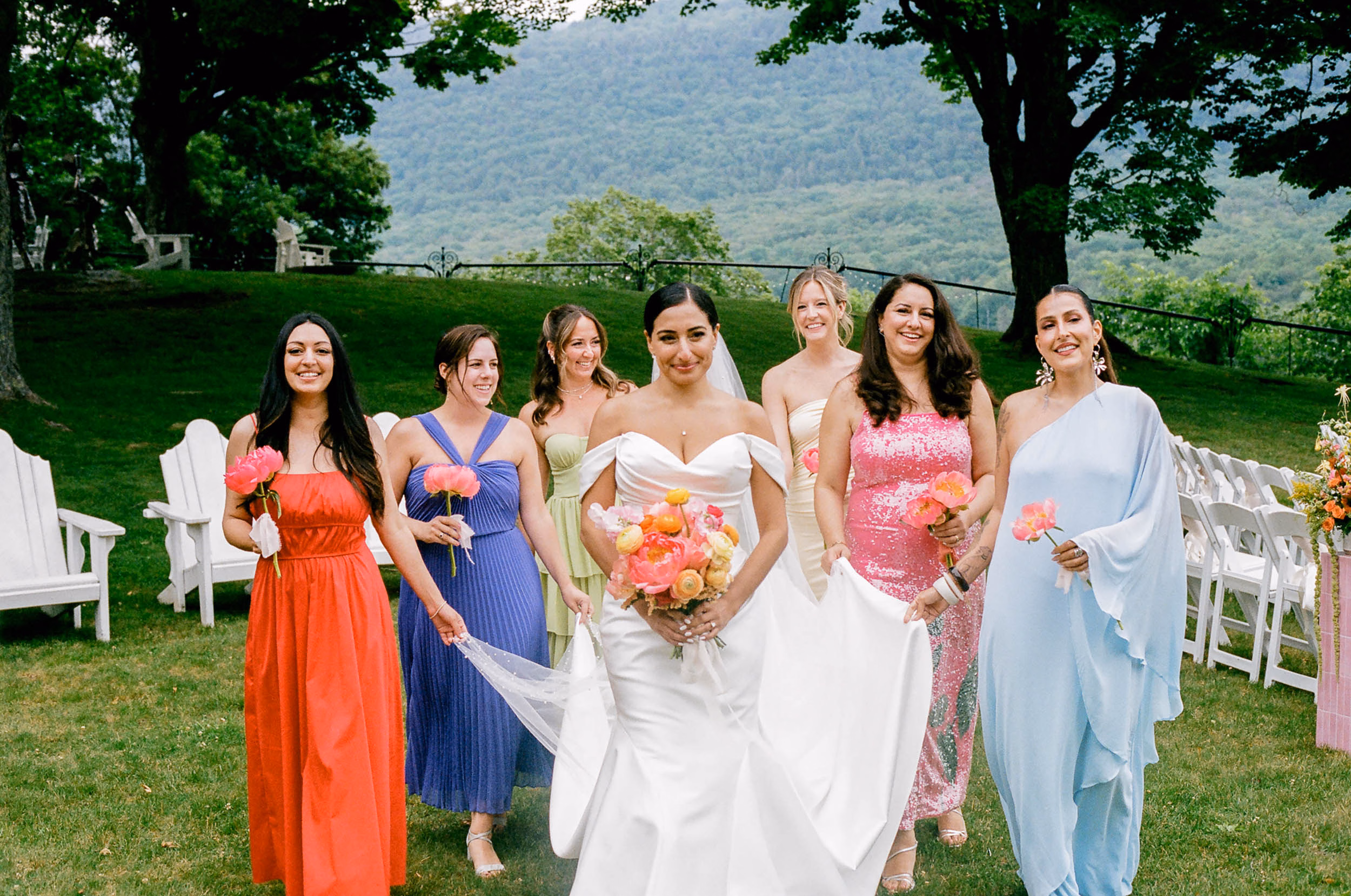 Modern Iranian bride carrying a colourful bouquet and surrounded by bridesmaids in different coloured dresses.